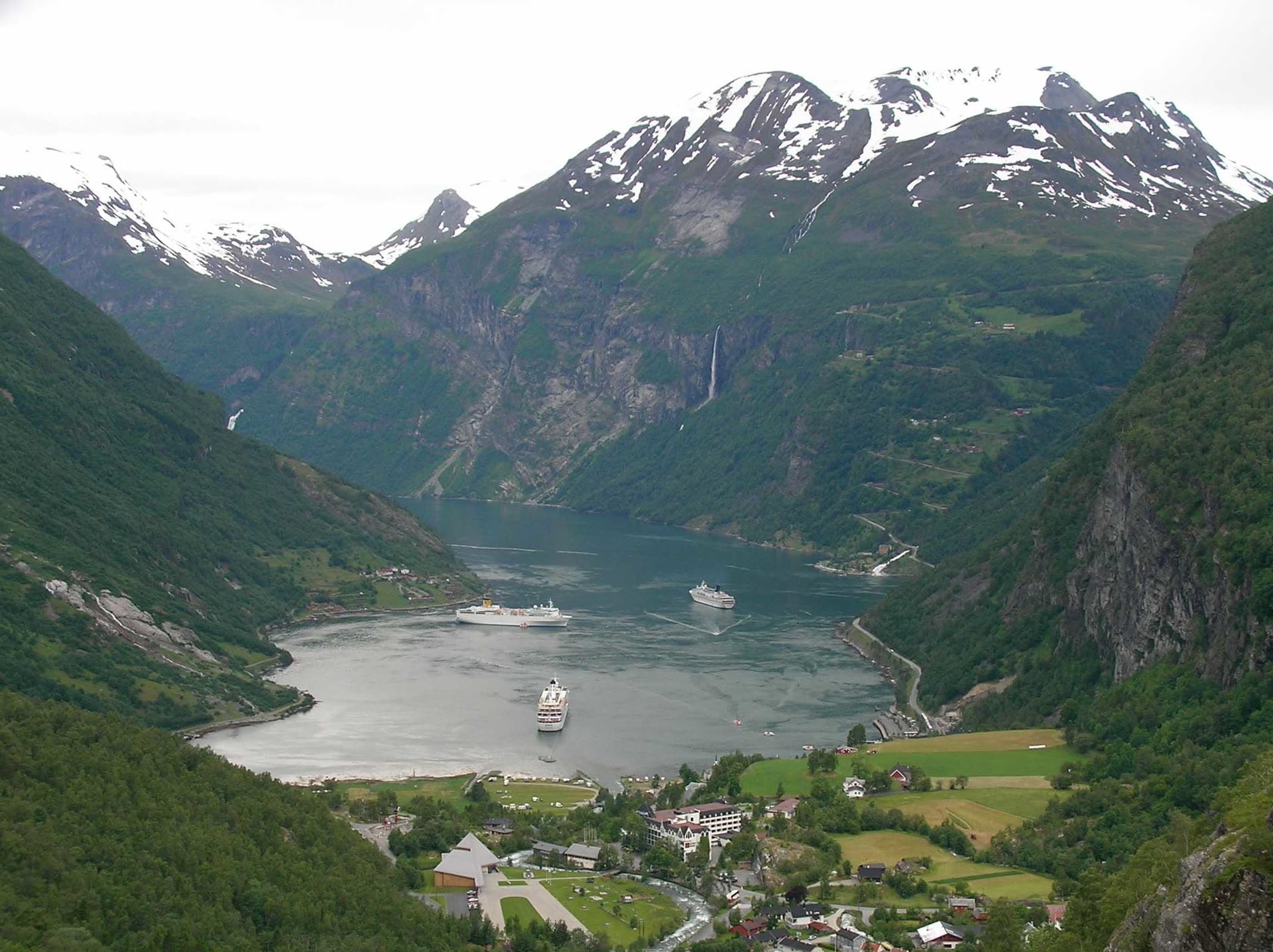 Ships on the Geirangerfjord between steep green mountains.